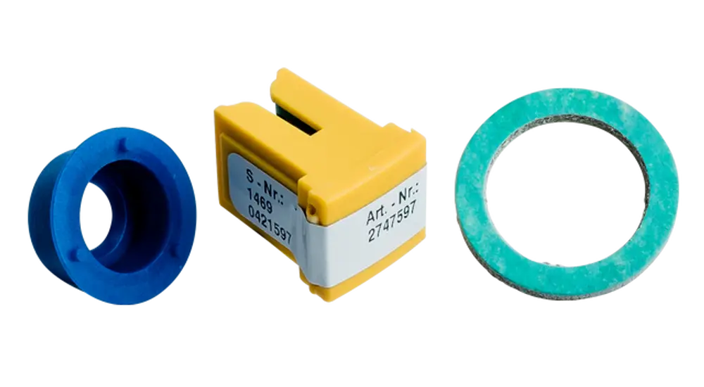 Drei Teile eines Umrüstsets von Wolf, bestehend aus einem blauen Ring, einem gelben Bauteil mit Aufschrift und einem grünen Dichtungsring.